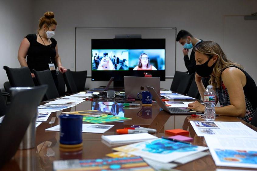 UMC employees working in a conference room with a zoom on the large screen showing a hybrid workspace.